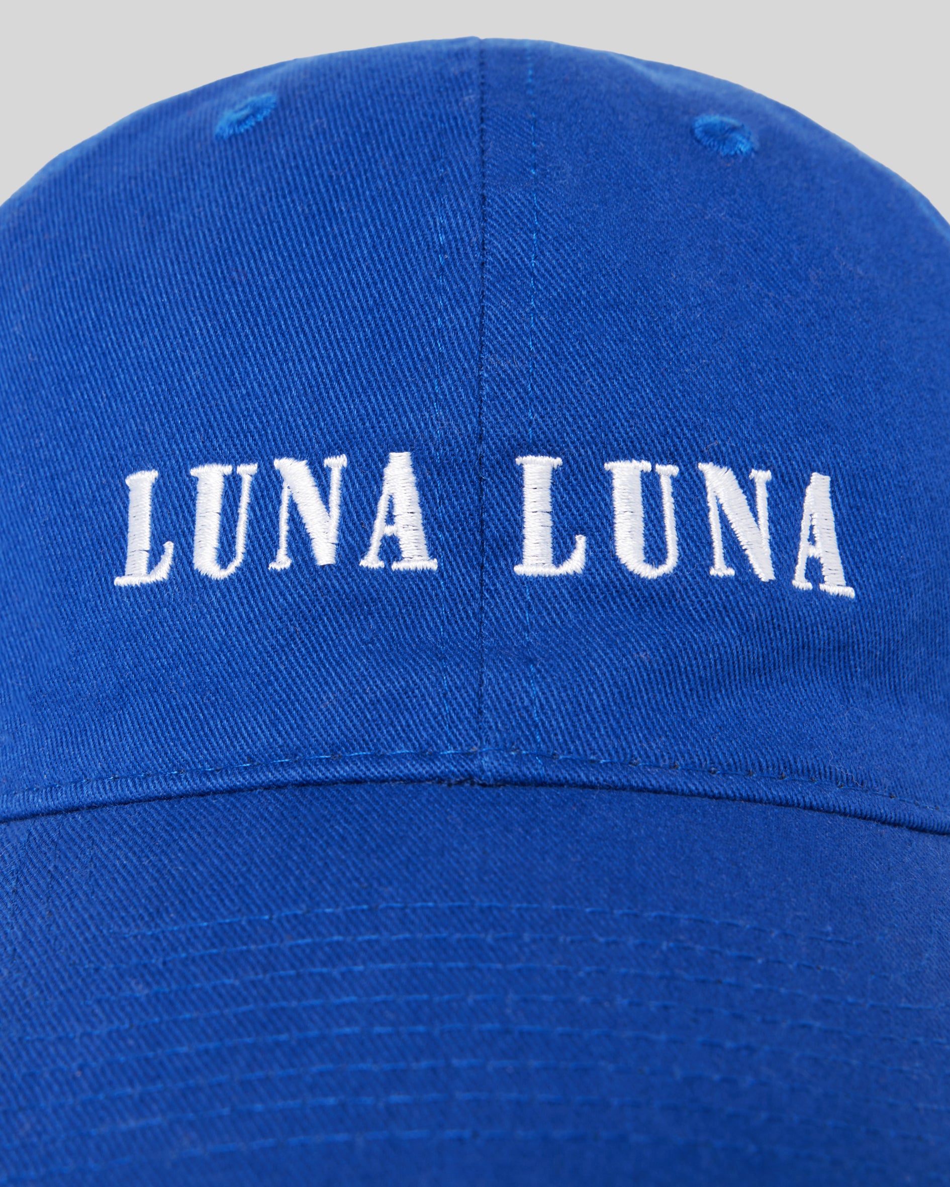 1987 Logo Hat, Cobalt Blue. Detail photograph of cobalt blue baseball hat with white Luna Luna embroidered text at front.